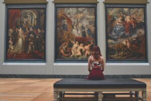 woman sitting on ottoman in front of three paintings