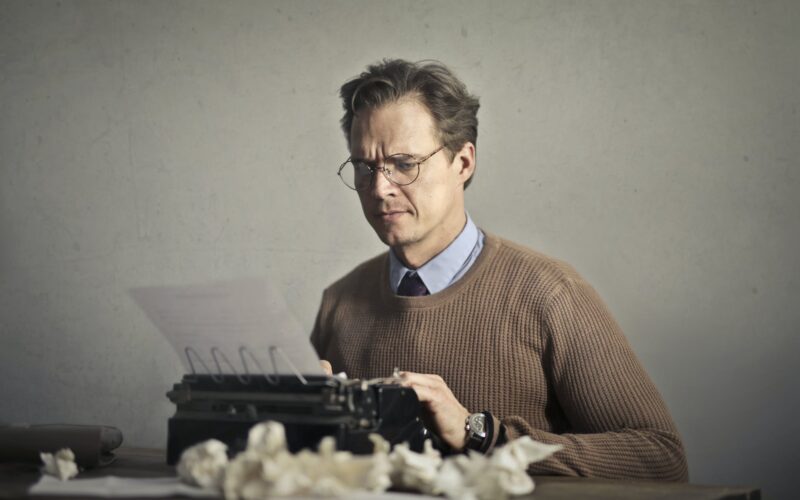 adult frowned male writer working on typewriter at home